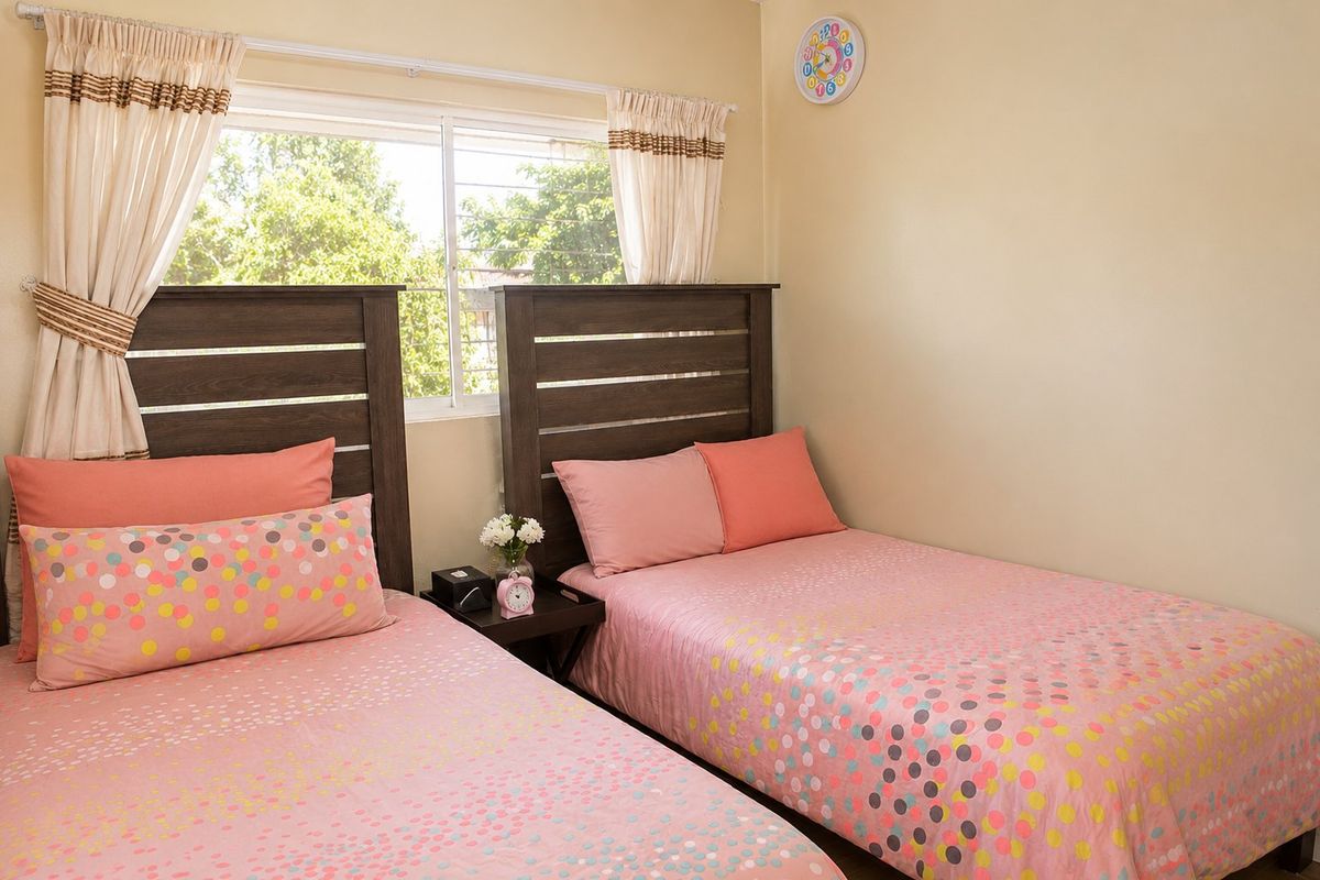A bedroom featuring two beds with a shared bedside table and a window with curtain tracks.