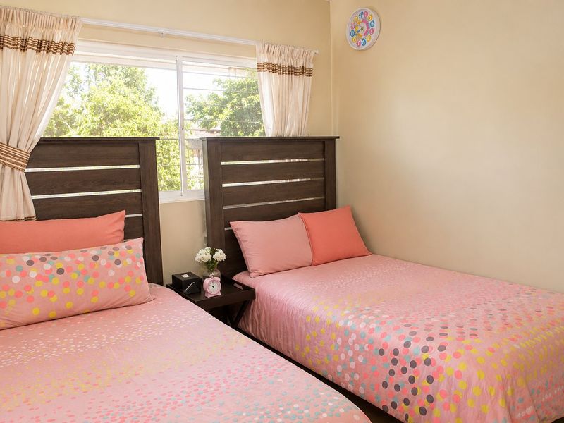 A bedroom featuring two beds with a shared bedside table and a window with curtain tracks.
