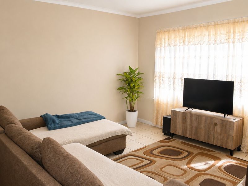 A comfortable living room featuring neutral wall tones, tiled flooring, and natural light filtering through window curtains.