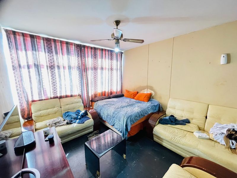 A bedroom featuring a ceiling fan and large window with curtains, requiring cosmetic updates to the wall finishes.