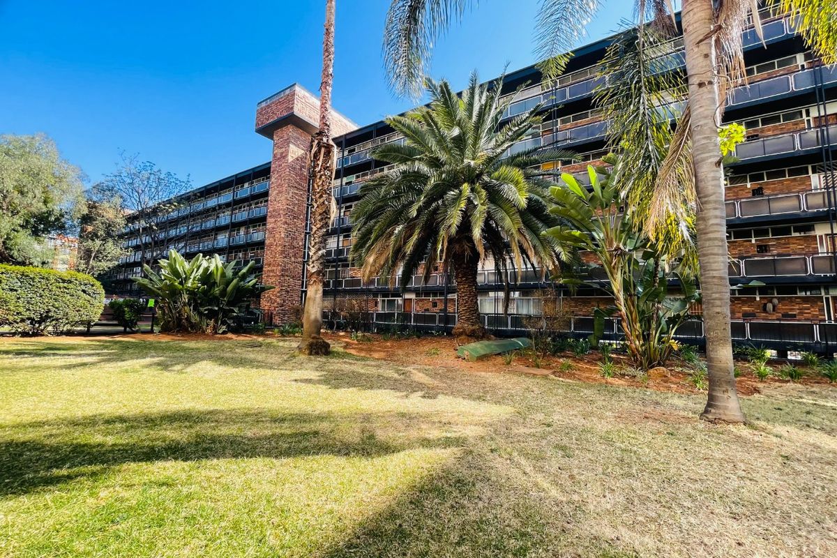 A view of the apartment building's rear facade featuring multiple balconies with metal railings, set against a well-maintained garden area.