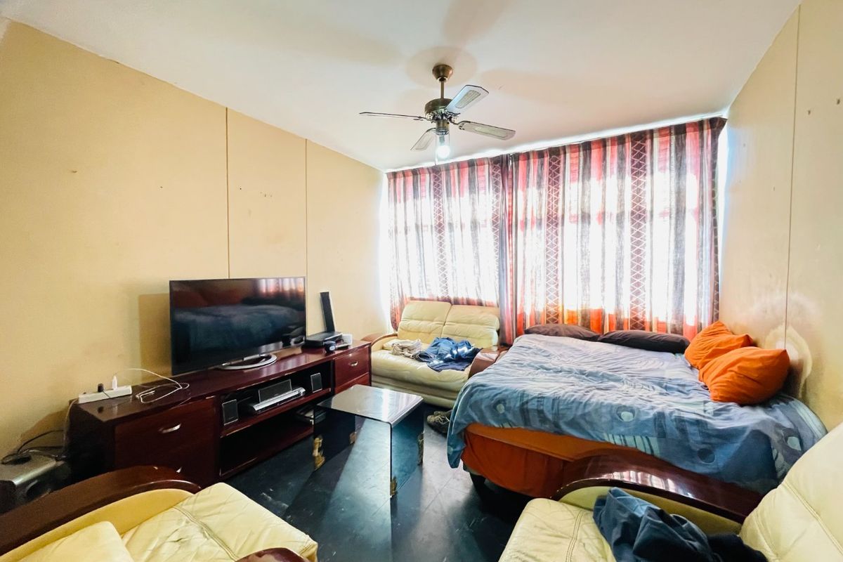 A living room area featuring a ceiling fan and large window with curtains, requiring cosmetic updates to improve the overall condition of the space.