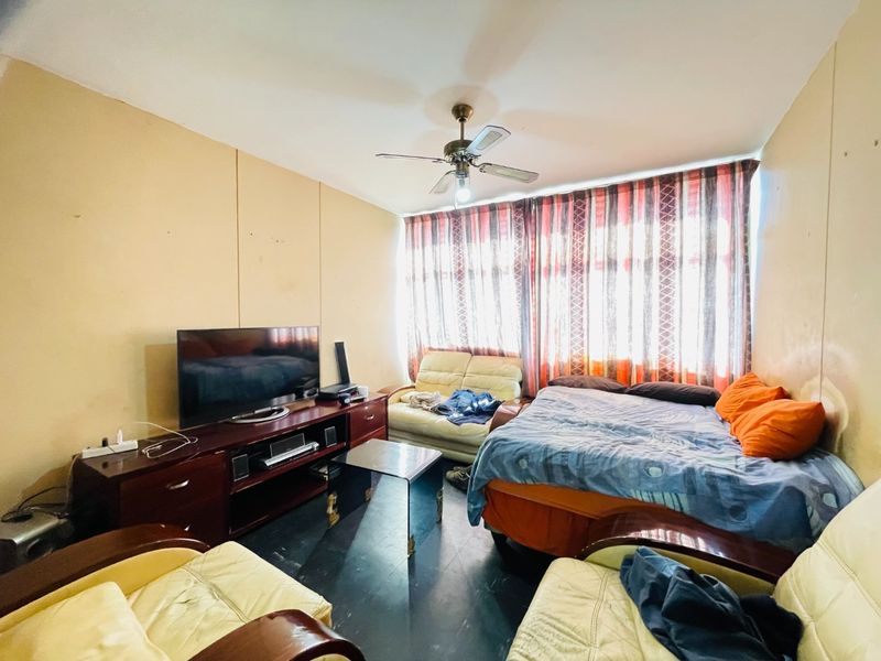 A living room area featuring a ceiling fan and large window with curtains, requiring cosmetic updates to improve the overall condition of the space.