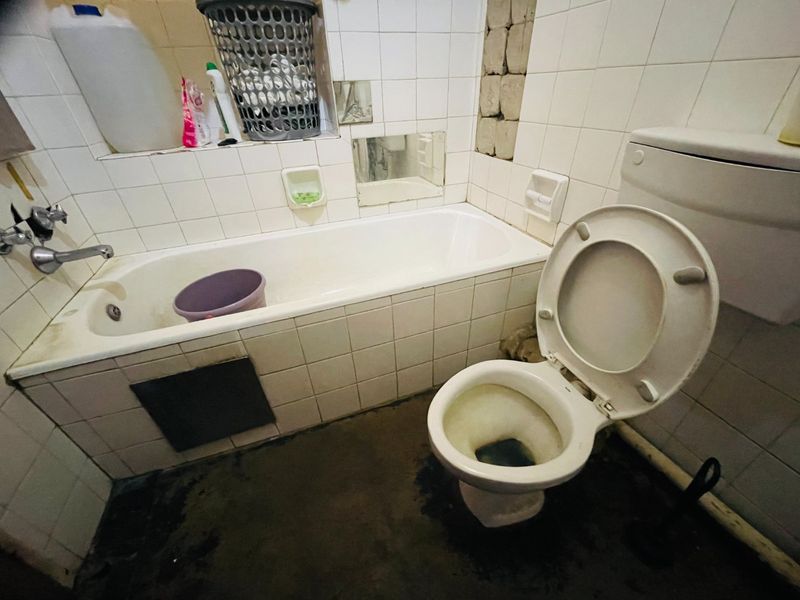 A dated bathroom featuring a bathtub and toilet with significant wear, missing wall tiles, and stained flooring requiring renovation.