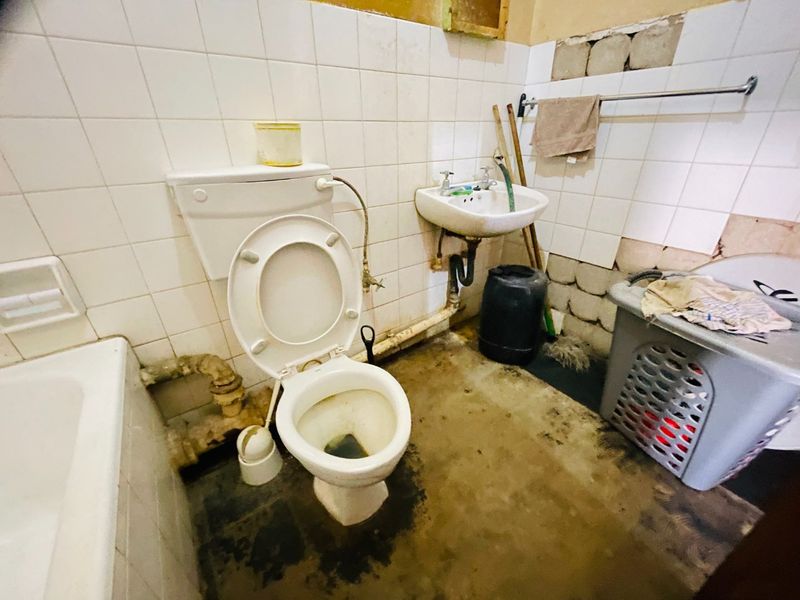 A bathroom in need of significant renovation, featuring a bathtub, toilet, and wall-mounted basin with visible damage to wall tiles and flooring.