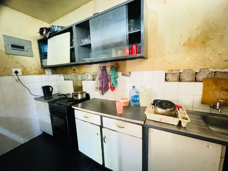 A dated kitchen featuring basic cabinetry, a stainless steel sink, and a freestanding stove, requiring significant cosmetic updates and wall repairs.
