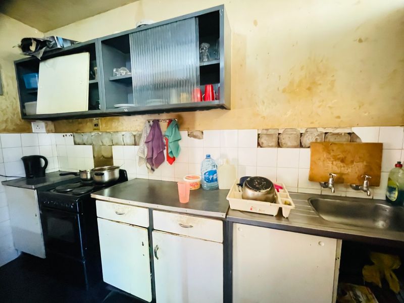 A dated kitchen featuring built-in cabinetry, a stainless steel sink, and an electric stove, requiring significant renovation and cosmetic updates to the walls and finishes.