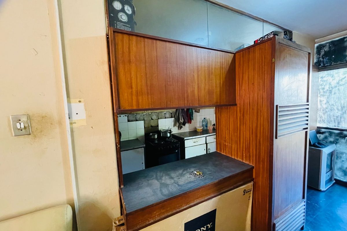 A dated kitchen area featuring original wooden cabinetry, a tiled backsplash, and a functional stove, offering significant potential for modernization and renovation.