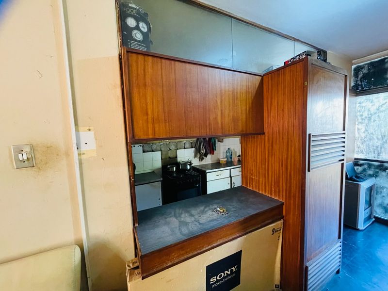 A dated kitchen area featuring original wooden cabinetry, a tiled backsplash, and a functional stove, offering significant potential for modernization and renovation.