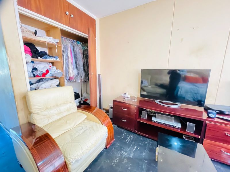 A bedroom featuring a built-in wardrobe with open shelving and hanging space, requiring cosmetic updates to the wall finishes.