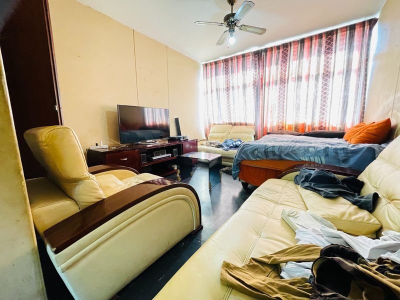 A living room space featuring a ceiling fan and large window area with curtains, requiring cosmetic updates to improve the overall condition.