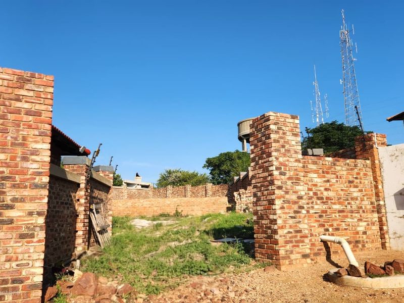 A view of a vacant residential plot enclosed by face brick boundary walls with installed electric fencing and basic drainage infrastructure.
