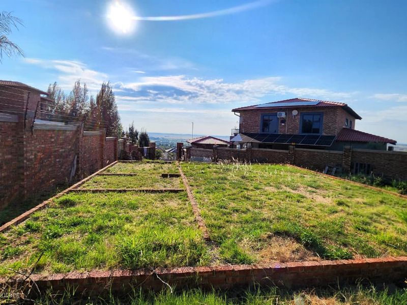 A vacant residential plot featuring a brick foundation slab, enclosed by brick boundary walls with electric fencing, offering a view of the surrounding area.