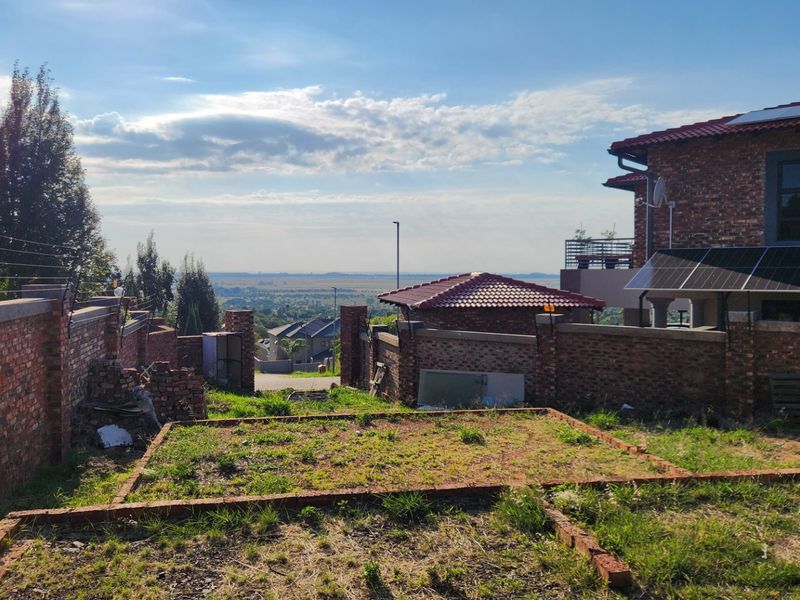 A view of a residential backyard featuring a brick boundary wall with electric fencing, solar panels on the roof, and an unfinished garden area.