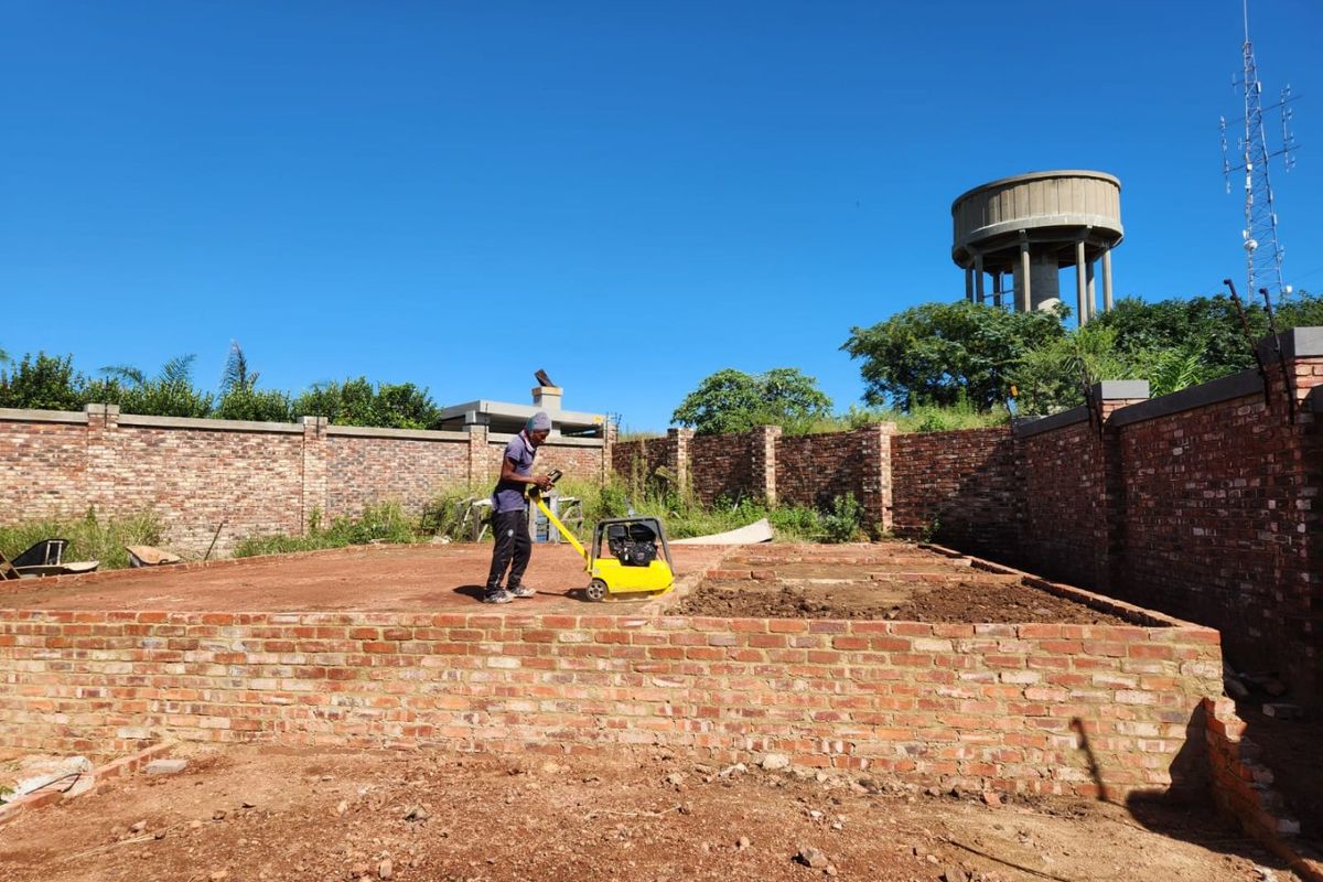 A vacant residential plot under development, featuring a brick perimeter wall and foundation work in progress.