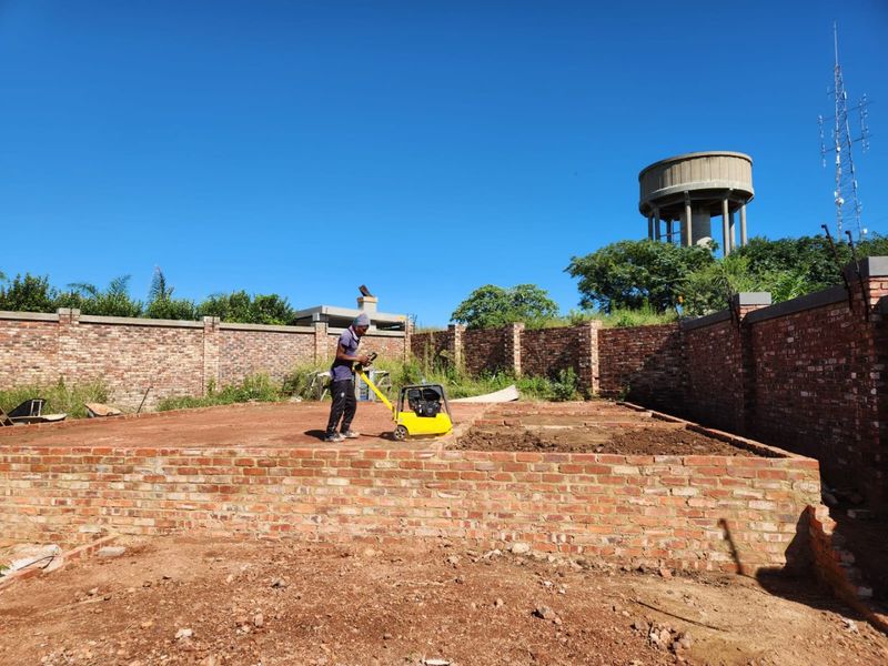 A vacant residential plot under development, featuring a brick perimeter wall and foundation work in progress.