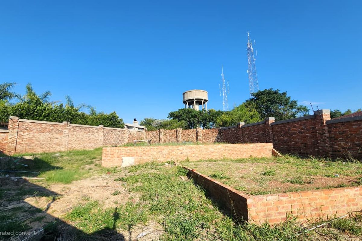 A vacant residential plot featuring a brick perimeter wall and a raised brick foundation slab, ready for development.