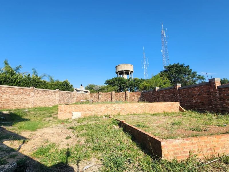A vacant residential plot featuring a brick perimeter wall and a raised brick foundation slab, ready for development.