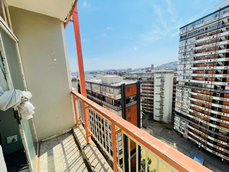 An outdoor balcony featuring a metal railing and tiled flooring, offering an elevated urban view of the surrounding apartment buildings.