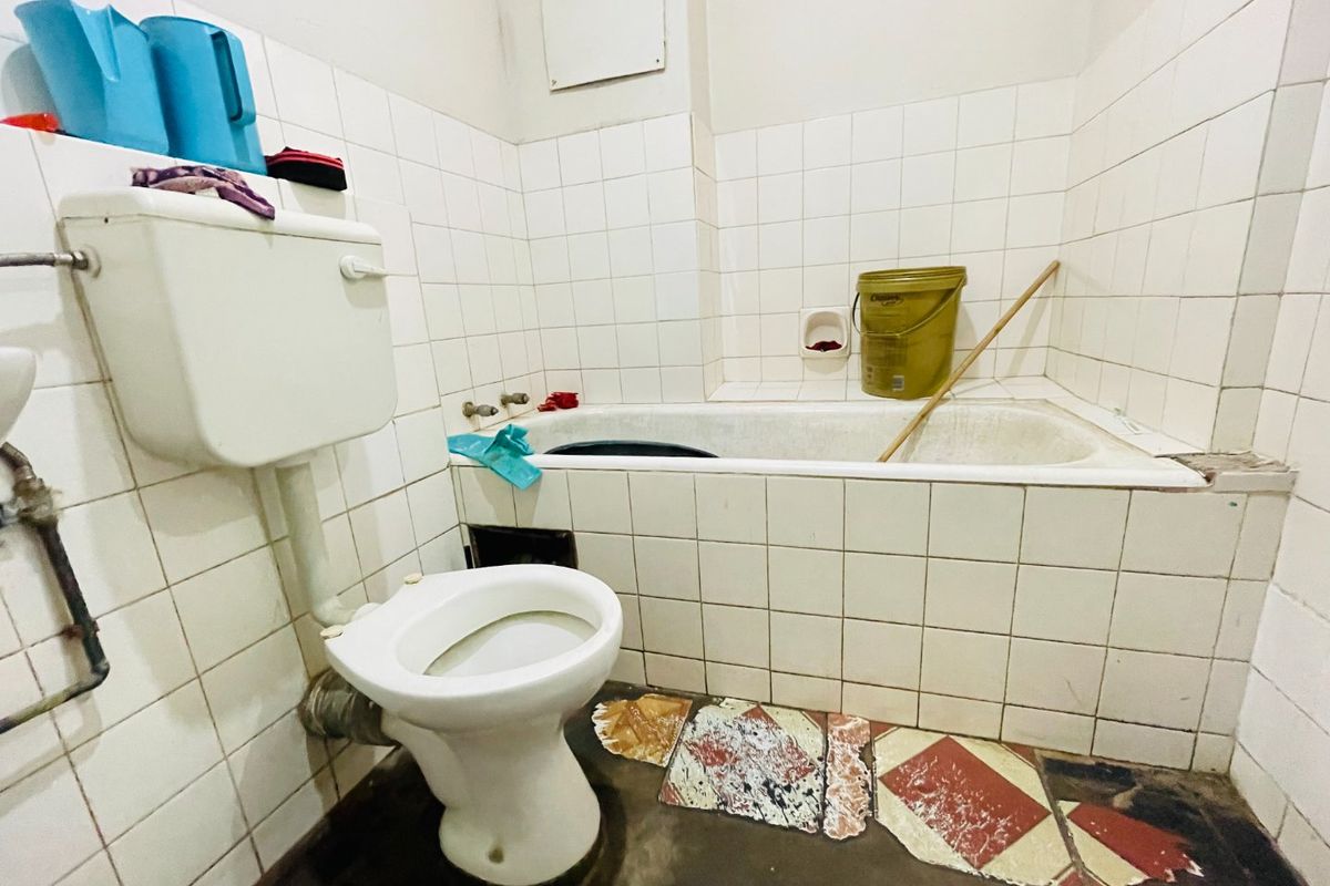 A dated bathroom featuring a standard toilet and bathtub with tiled walls, requiring significant renovation and repair to the flooring and fixtures.