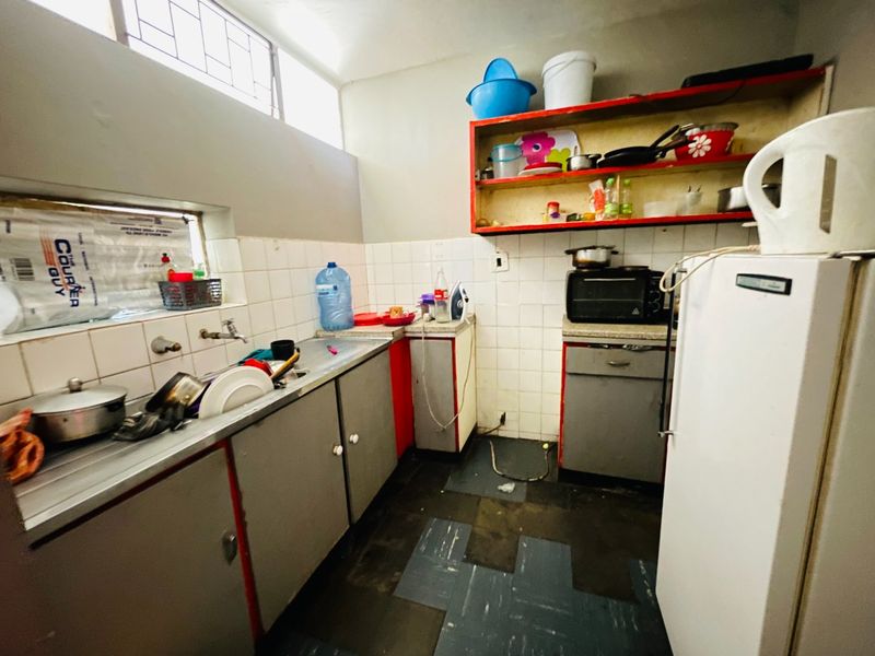 A compact kitchen featuring a stainless steel sink, tiled backsplash, and built-in cabinetry, requiring cosmetic updates to improve its overall condition and functionality.