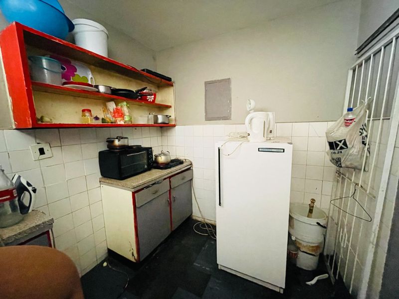 A compact kitchen area featuring basic cabinetry, tiled splashbacks, and a functional layout in need of cosmetic updates and modernization.