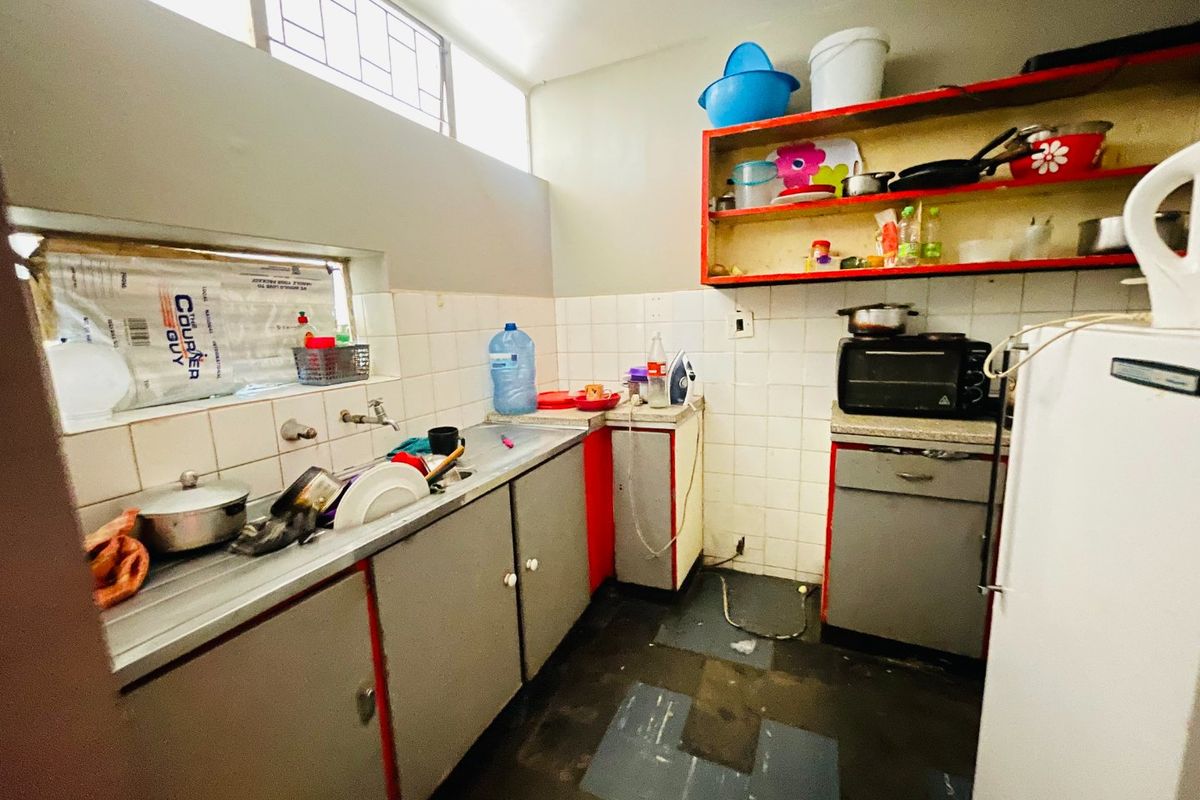 A compact kitchen featuring built-in cabinetry, a stainless steel sink, and tiled backsplash, requiring cosmetic updates to improve its overall condition and functionality.