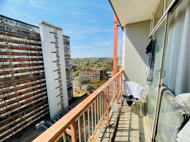 A balcony featuring a metal railing and tiled flooring, offering an elevated urban view of the surrounding apartment complex and neighborhood.