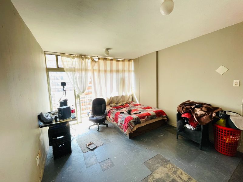A bedroom featuring tiled flooring and a sliding glass door providing natural light. The space requires cosmetic updates to improve its overall condition.