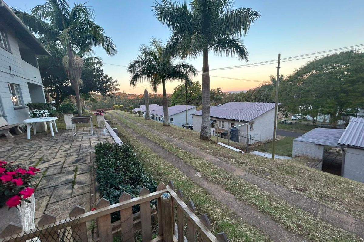 A rear exterior view of the property featuring a paved patio area, established palm trees, and a view over the surrounding residential grounds.