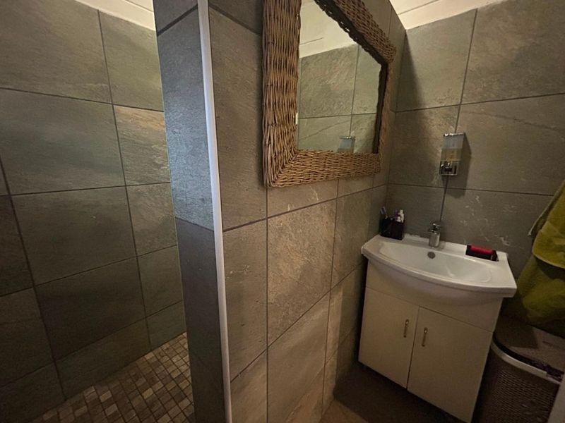 A compact bathroom featuring a vanity cabinet with a basin, tiled walls, and a separate shower enclosure with mosaic floor tiling.