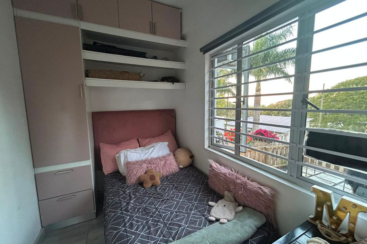 A compact bedroom featuring built-in wardrobe cabinetry, overhead storage, open shelving, and a window fitted with security bars.
