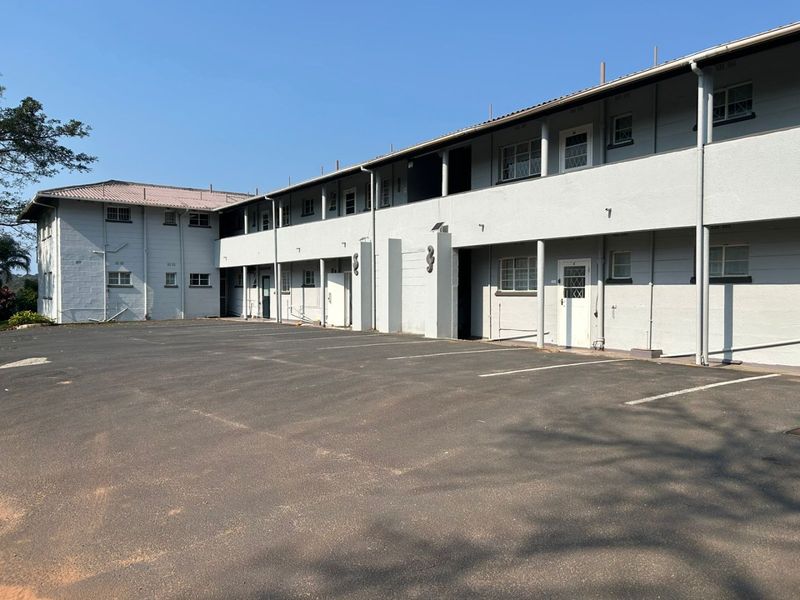 Exterior view of a multi-story apartment complex featuring a paved parking area and covered walkways providing access to individual units.