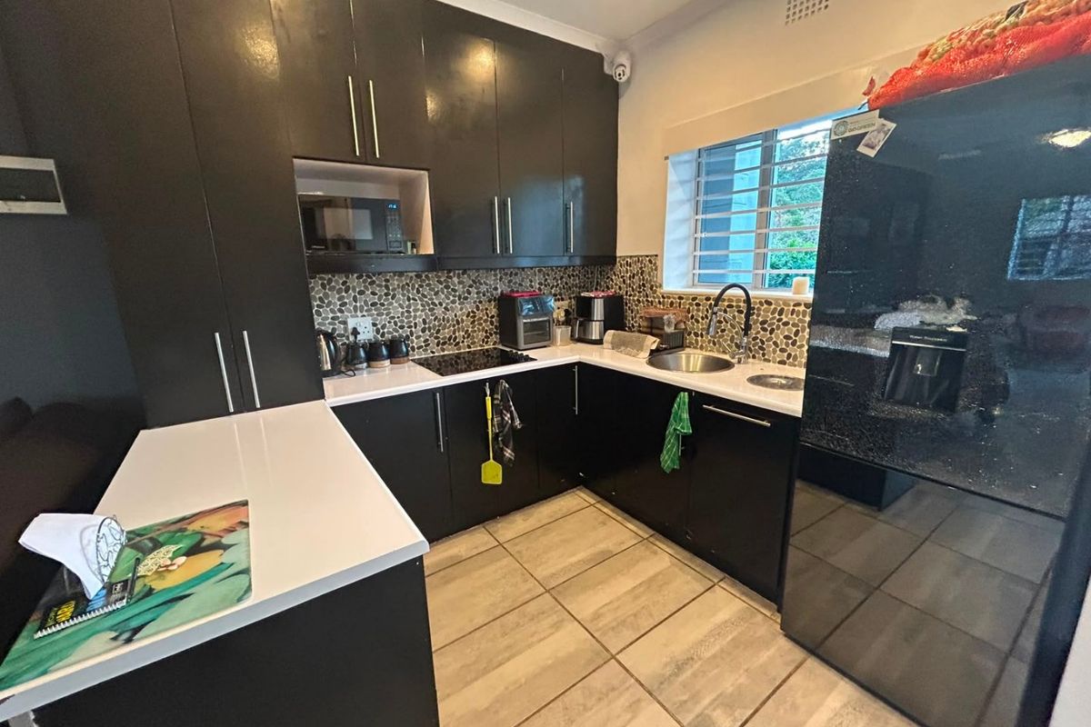 Modern kitchen featuring dark cabinetry, stone countertops, a unique pebble mosaic backsplash, and integrated appliances, complemented by neutral tiled flooring.