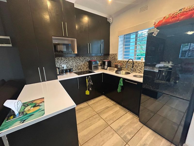 Modern kitchen featuring dark cabinetry, stone countertops, a unique pebble mosaic backsplash, and integrated appliances, complemented by neutral tiled flooring.