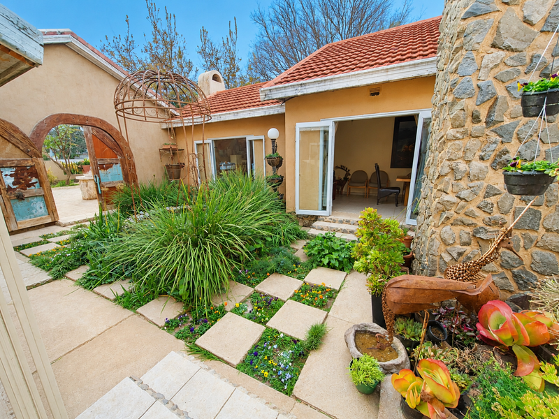 A charming rear courtyard featuring stone-clad walls, terracotta roof tiles, and a landscaped garden with paved pathways leading to the main living area.