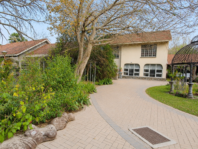 Front view of the property featuring a paved driveway, mature trees, and a detached wrought iron gazebo structure.