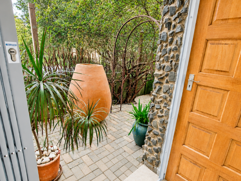 A view from an interior doorway onto a paved patio area featuring stone wall cladding, a timber door, and a metal garden arch.