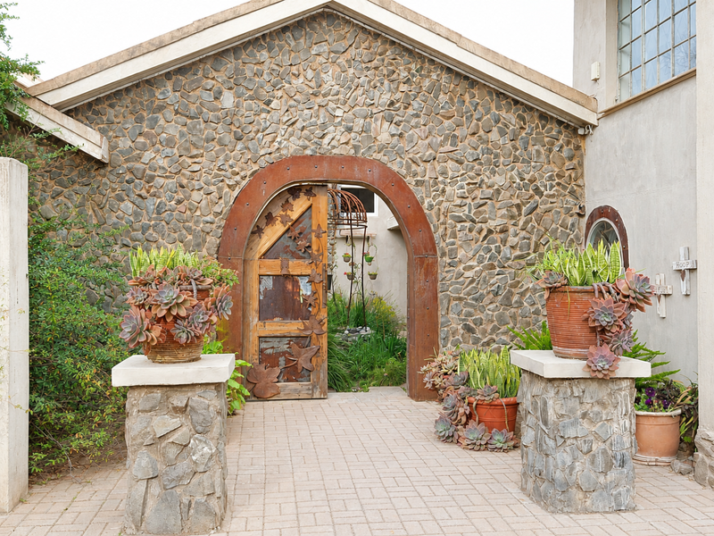A unique front entrance featuring a stone-clad facade, an arched doorway with a custom metal door, and stone pillars leading to the main entry.