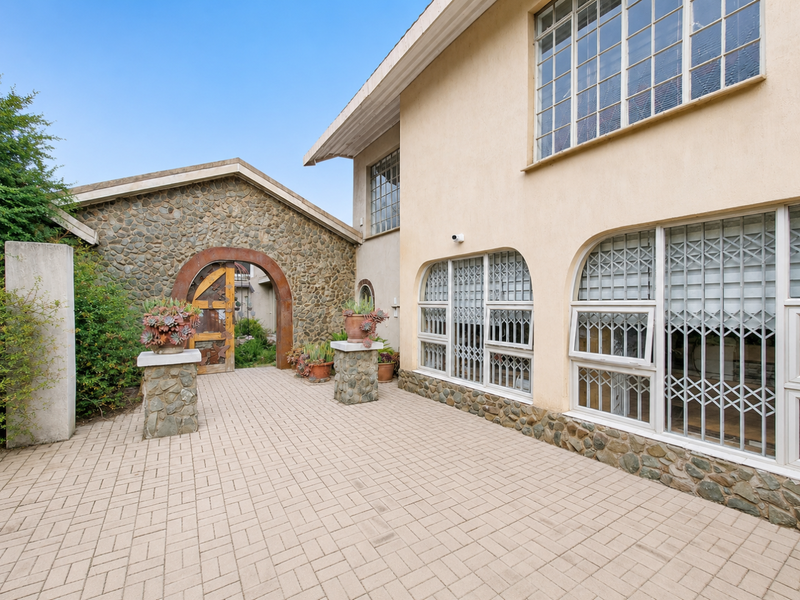 A rear exterior view featuring a paved patio area, stone-clad wall accents, and secure arched entrance with decorative metalwork.