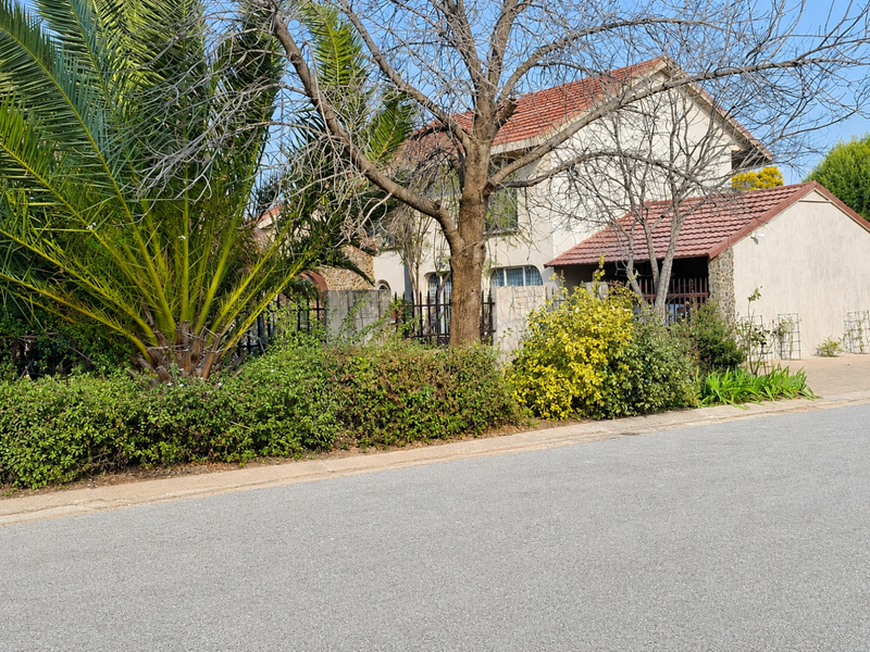 Front elevation of a two-story house featuring a tiled roof, stone cladding accents, and established garden landscaping with a paved driveway.