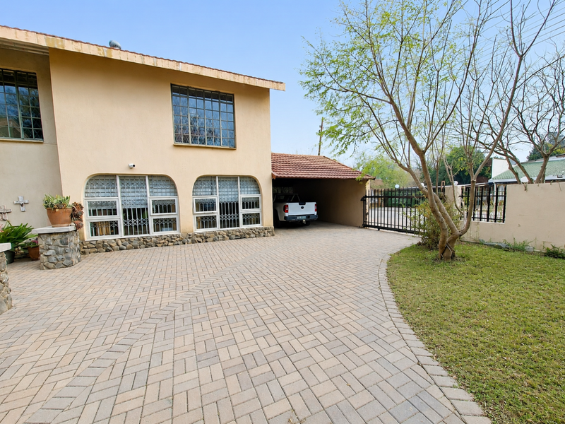 Front exterior view of the house featuring a paved driveway, attached carport, security gates, and stone-clad accents on the facade.
