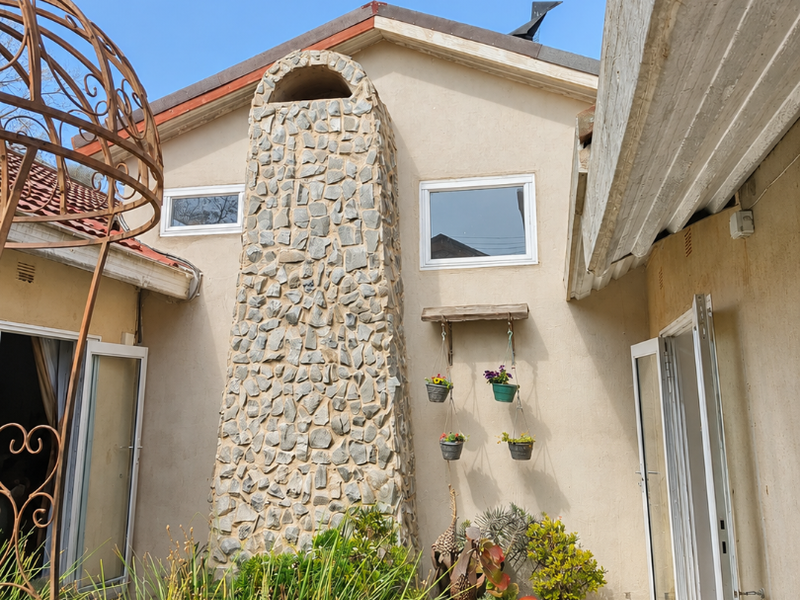 Rear courtyard area featuring a prominent stone-clad chimney, tiled patio access, and direct entry into the home through double glass doors.