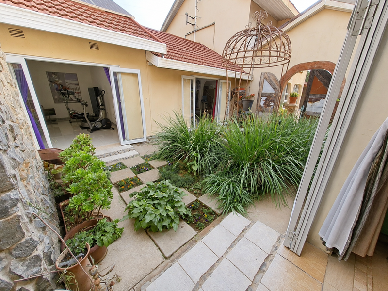 A private rear courtyard featuring stone-clad walls, paved pathways, landscaped garden beds, and bi-fold doors providing seamless access to the interior living spaces.