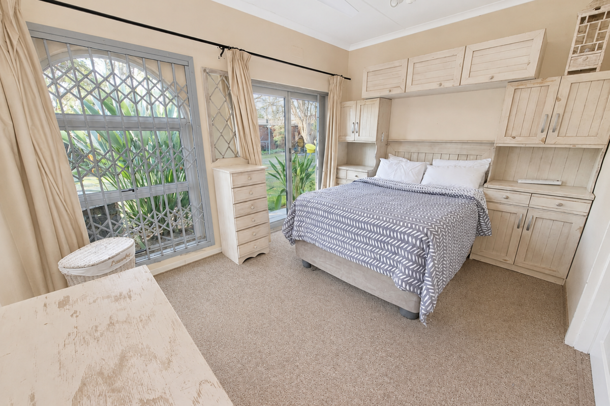 A bedroom featuring built-in cabinetry, carpeted flooring, and a sliding glass door with a security gate providing access to the garden.