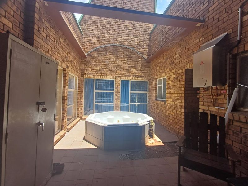 An enclosed outdoor patio area featuring exposed brick walls, tiled flooring, and a built-in spa bath, offering a private space for relaxation.