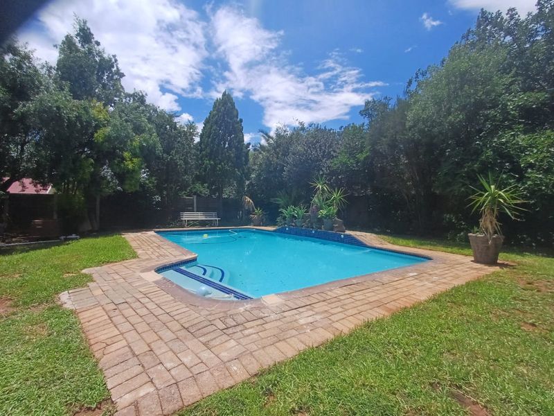A well-maintained outdoor swimming pool area featuring brick paving surround and established garden landscaping.
