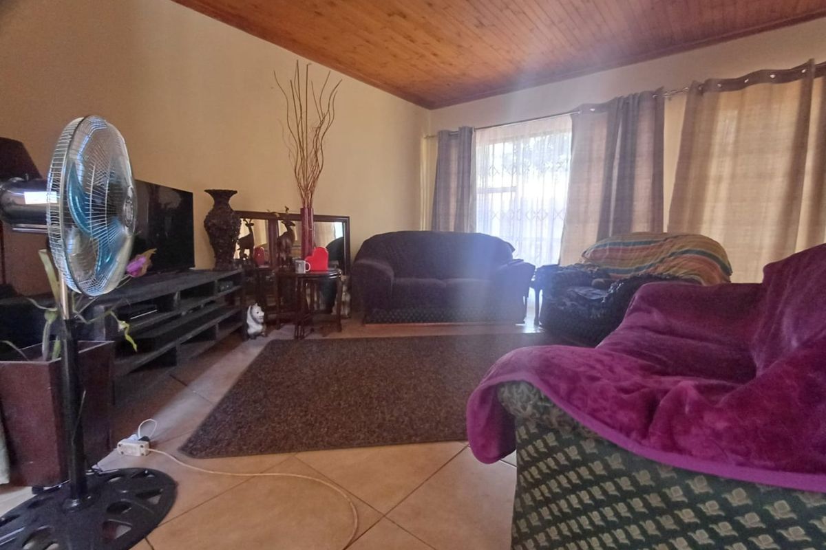 A living room featuring tiled flooring and a timber-paneled ceiling, with a large window providing natural light.