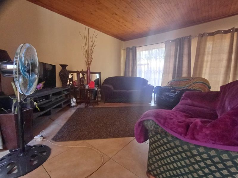 A living room featuring tiled flooring and a timber-paneled ceiling, with a large window providing natural light.