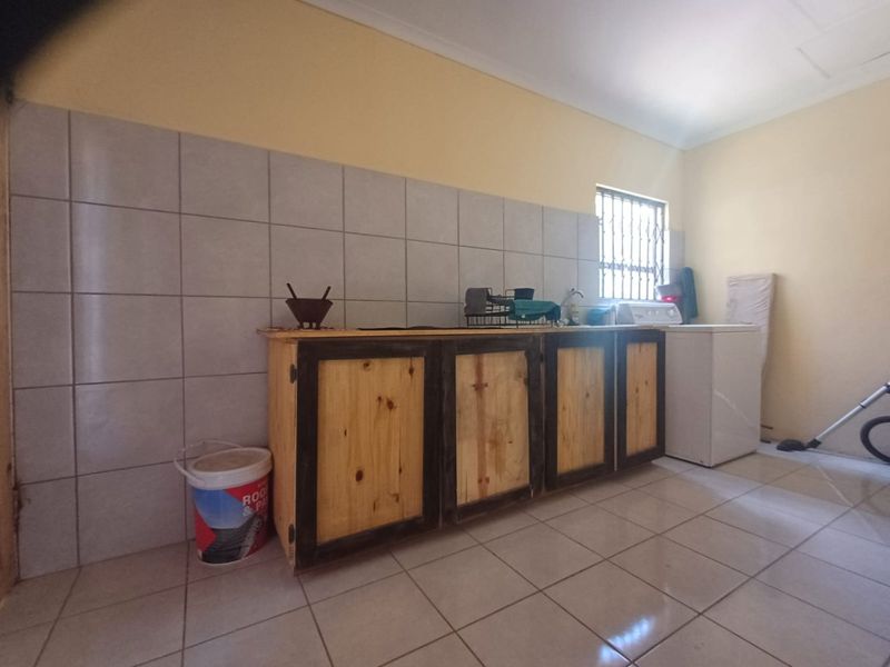 A functional laundry area featuring tiled splashbacks, tiled flooring, and custom wooden cabinetry with security bars on the window.